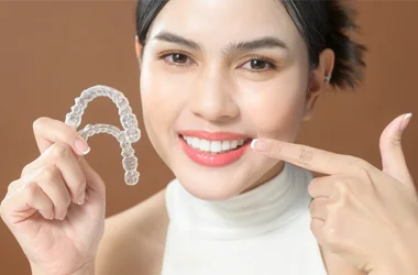 Dentist Oceanside CA Orthodontics HP A woman holding clear aligners points to her now straight smile